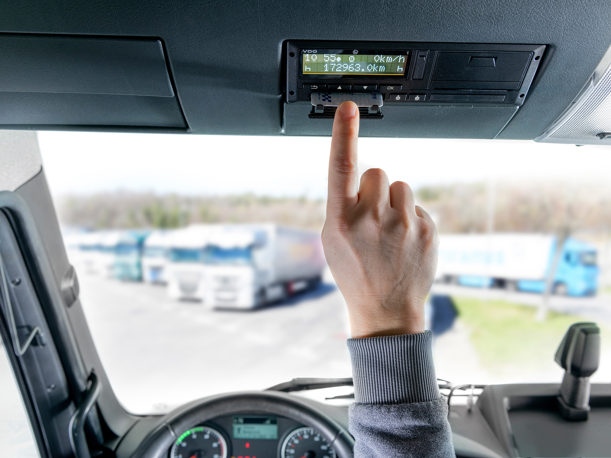 Ein Fahrer steckt seine Fahrerkarte in den VDO DCTO 4.1 - den intelligenten Tachographen der zweiten Version. Durch die Windschutzscheibe sind im Hintergrund unscharf weitere Lkw der Flotte zu erkennen.